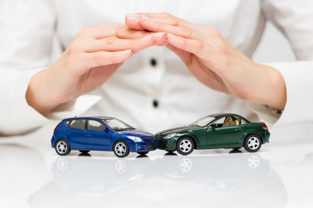 Dois veículos e mãos protegendo uma miniatura de carro